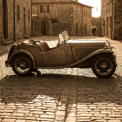 Automotive wall art, a sepia vintage roadster in side profile on a cobblestone street in warm evening light