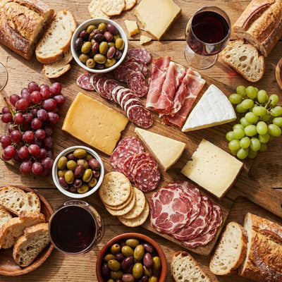 Food wall art, overhead view of a charcuterie spread with cheeses, grapes, olives, bread and red wine on a wooden table
