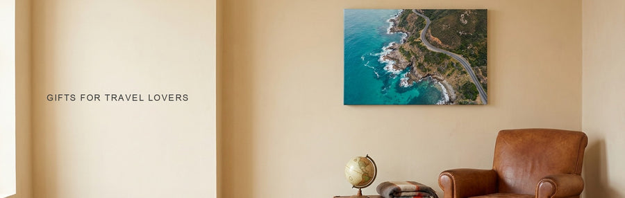 Gifts for travel lovers: a cozy reading corner with a leather armchair, a vintage suitcase and a turquoise coastline canvas on the wall