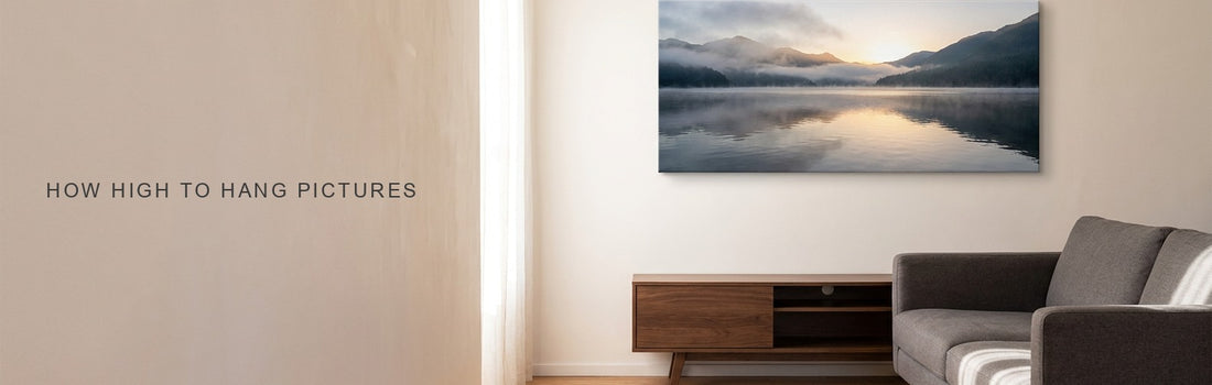 How high to hang pictures: a living room with a gray sofa and walnut console and a calm lake and mountain sunrise canvas centered above them