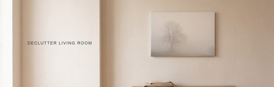 Declutter living room result: a tidy minimalist living room with a low oak bench and a quiet landscape of a single tree in fog
